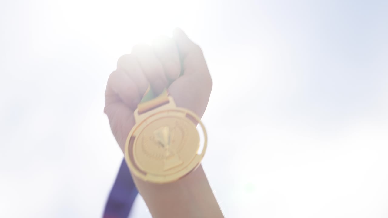 Raised hand holding medal against sky in outdoor scene. Concept of achievement, success, victory, motivation, and recognition. Symbol of winning and personal accomplishment