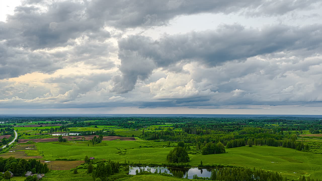 Patchy clouds drift over green countryside with sunlit grassy meadows, static timelapse overview