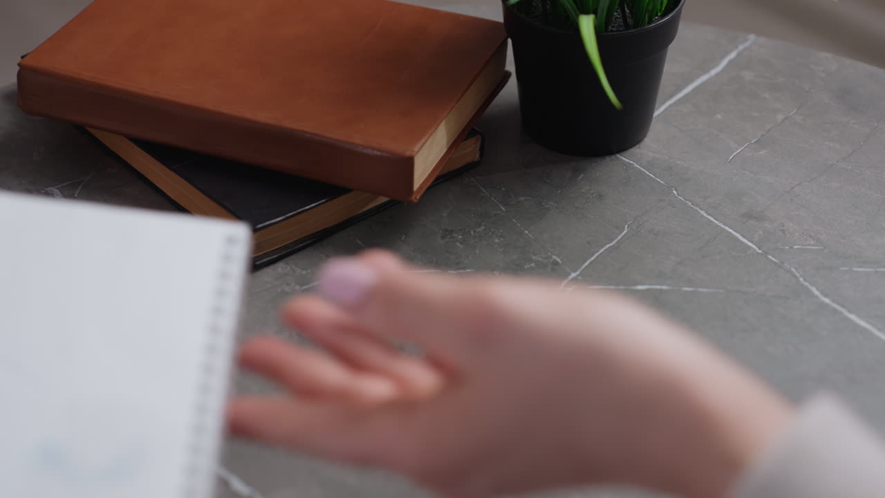 En piges og forældres hænder holder en notesbog under læringsprocessen med bøger og en grøn plante på skrivebordet, der symboliserer uddannelse, kreativitet, kommunikation, vejledning, disciplin og støtte i familien