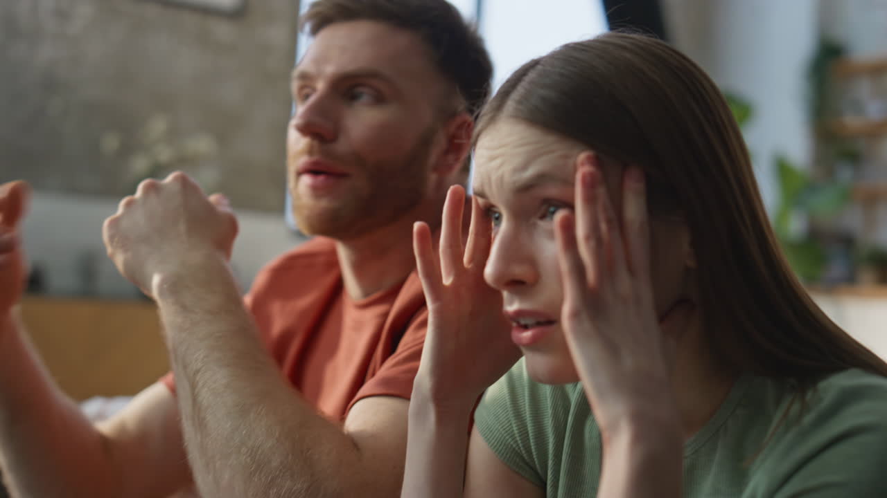 Worried spouses cheering football game at TV sitting couch dissatisfied closeup