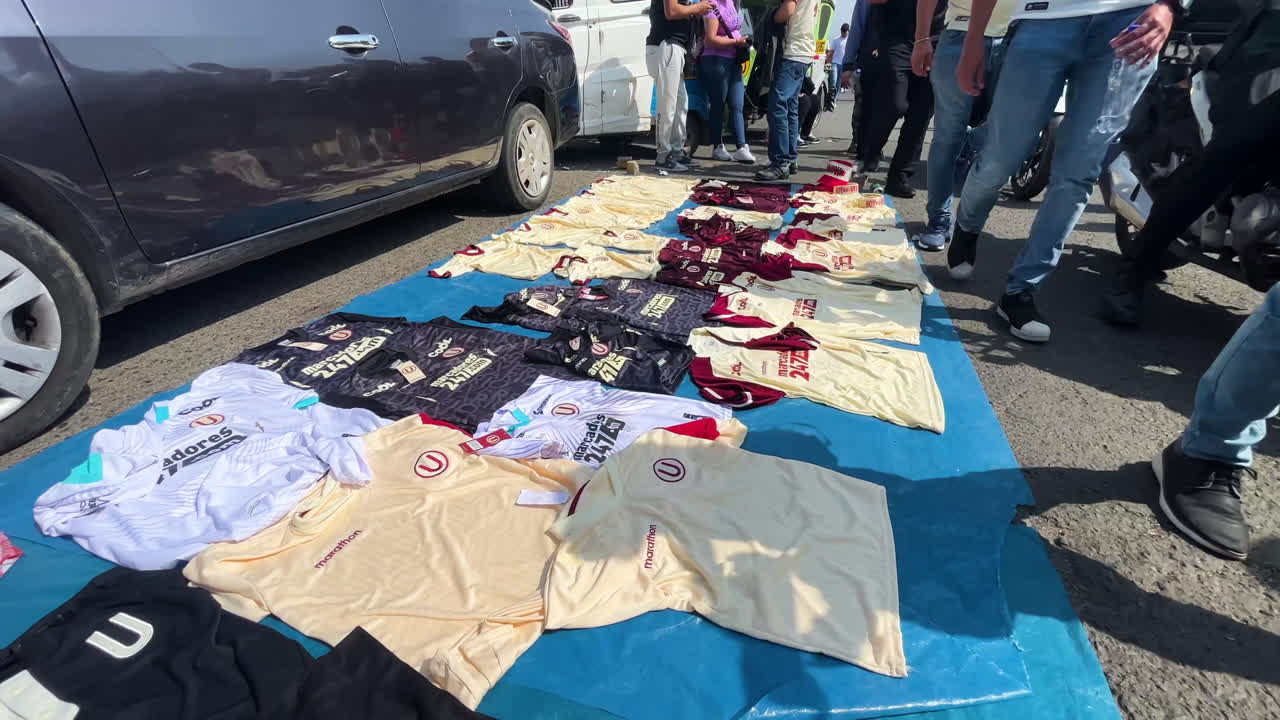 toma en ángulo alto sobre un vendedor al borde de la carretera que vende camisetas de fútbol a la venta antes de un partido en universitario, monumental, ate, lima, perú durante el día