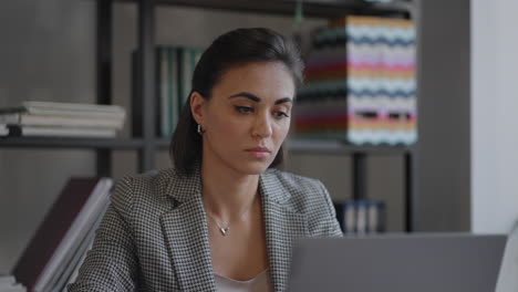 Una-Joven-Hermosa-Está-Sentada-En-Una-Silla-Y-Escribiendo-O-Tomando-Notas-Mientras-Asiste-A-Una-Clase-De-Video-En-Línea-O-A-Una-Reunión-De-Oficina-En-Una-Computadora-Portátil.-Mujer-Musulmana-Moderna-Que-Usa-Trabajos-En-Línea-De-Forma-Remota