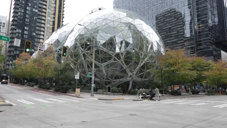 view of the spheres at amazon in seattle, with pedestrians crossing and cars passing along lenora street and 7th avenue. the iconic glass domes are surrounded by modern skyscrapers and urban greenery.