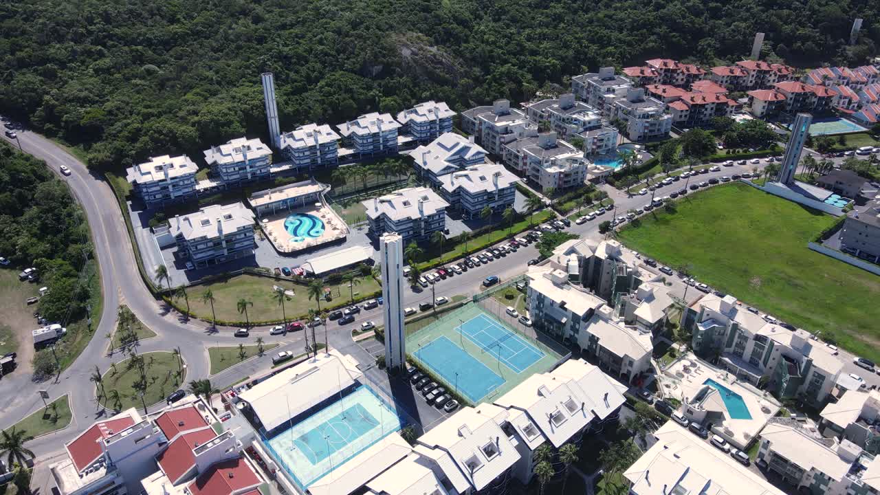 Aerial view of Praia Brava in Florianópolis with several apartment complexes and summer homes in front of the beach surrounded by mountains and Atlantic forest during the high summer season