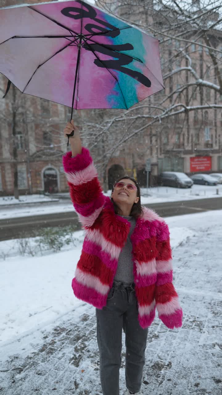 mujer con abrigo de piel rosa y paraguas en la ciudad nevada