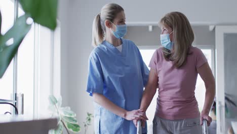 Female-health-worker-assisting-senior-woman-to-walk-with-walking-frame-at-home