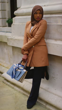 vertical video full length portrait of muslim businesswoman wearing hijab and modern business suit standing outside city office buildings 2