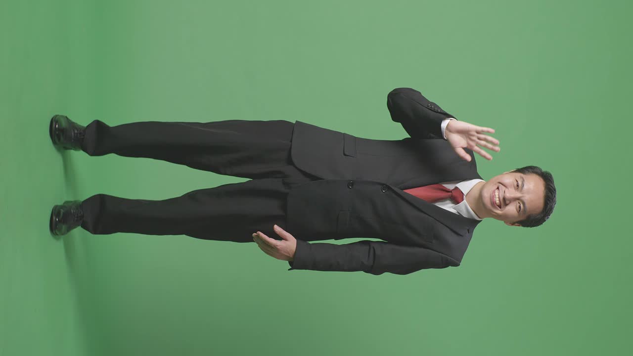 스튜디오에서 녹색 스크린에 서 있는 동안 손을 흔들고 미소 짓는 아시아 사업가의 몸이 가득 차 있습니다.