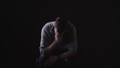 sitting, sad man sobs in dark room, black background