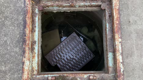 looking down into an open manhole showing sewer with waste water.