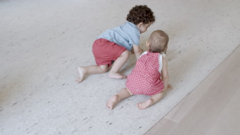 niños pequeños arrastrándose por el suelo para jugar a la pelota en la sala de estar.