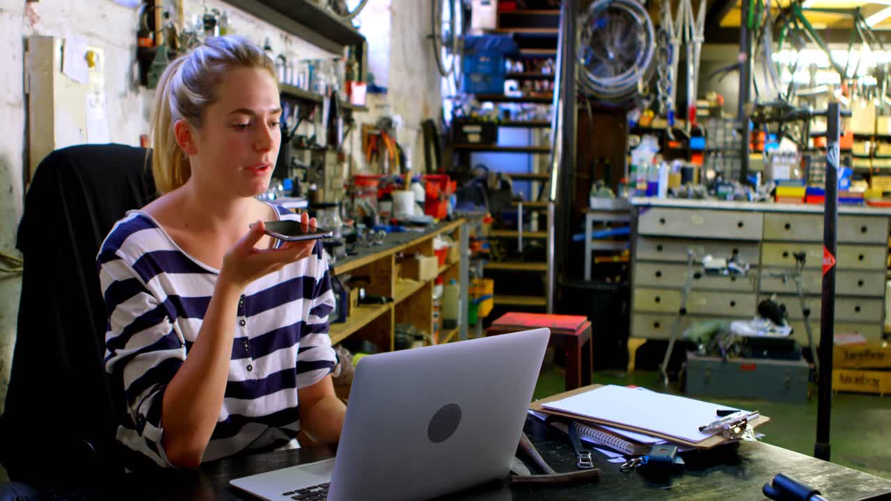 mujer hablando por teléfono móvil mientras usa una computadora portátil en el taller 4k