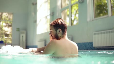 un joven padre feliz con barba está pasando el rato con su hijo pequeño en la piscina cerrada. girándolo por encima del agua. tiempo feliz juntos