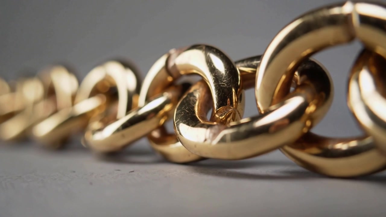 Moving macro camera shifting focus revealing polished gold link chain on gray table to show details