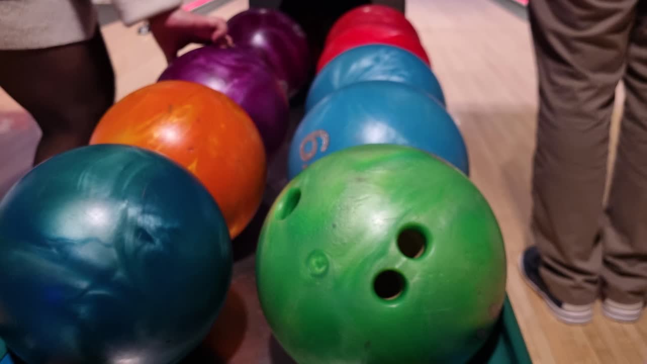 Le brillanti palle da bowling sono disposte in ordine sul supporto di ritorno all'interno di una pista da bowling, poco prima dell'inizio del gioco, creando un'invitante atmosfera di svago al chiuso mentre i giocatori si preparano a scegliere la loro attrezzatura.