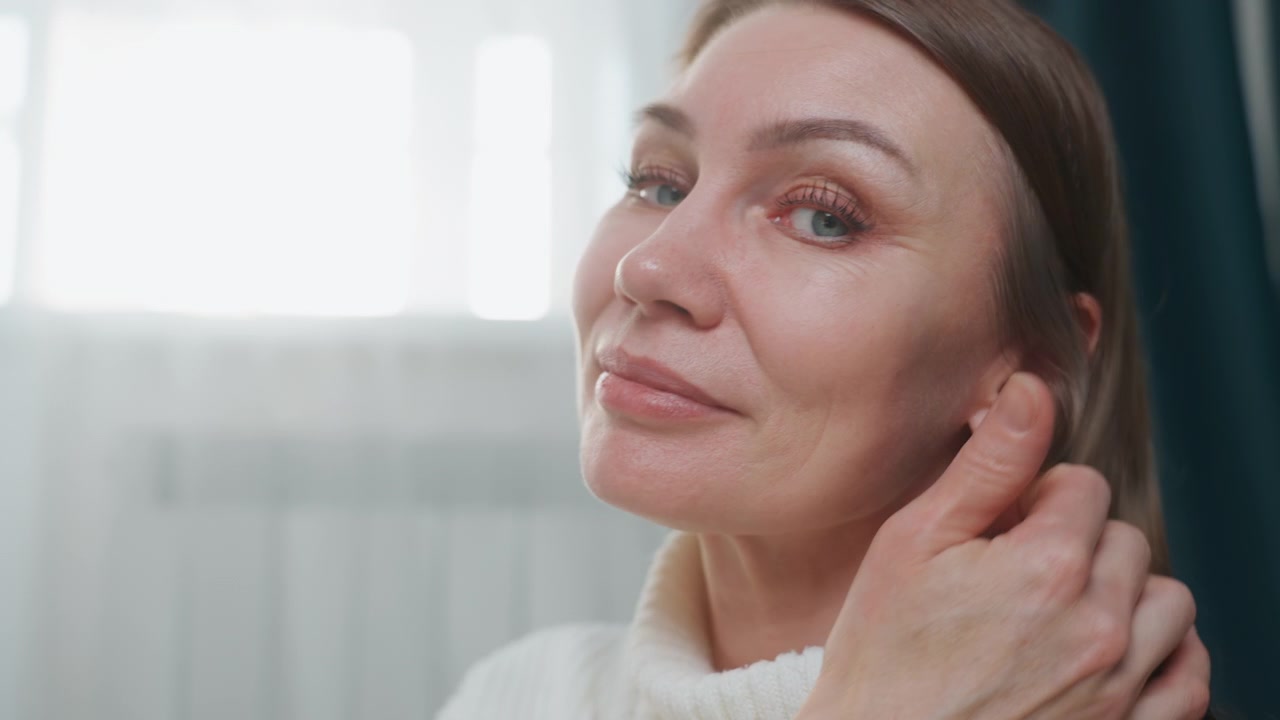Caucasian woman vocal coach smiling warmly, speech therapist guiding pronunciation and articulation, hand touching hair, close portrait with soft backlight from window, calm encouraging expression