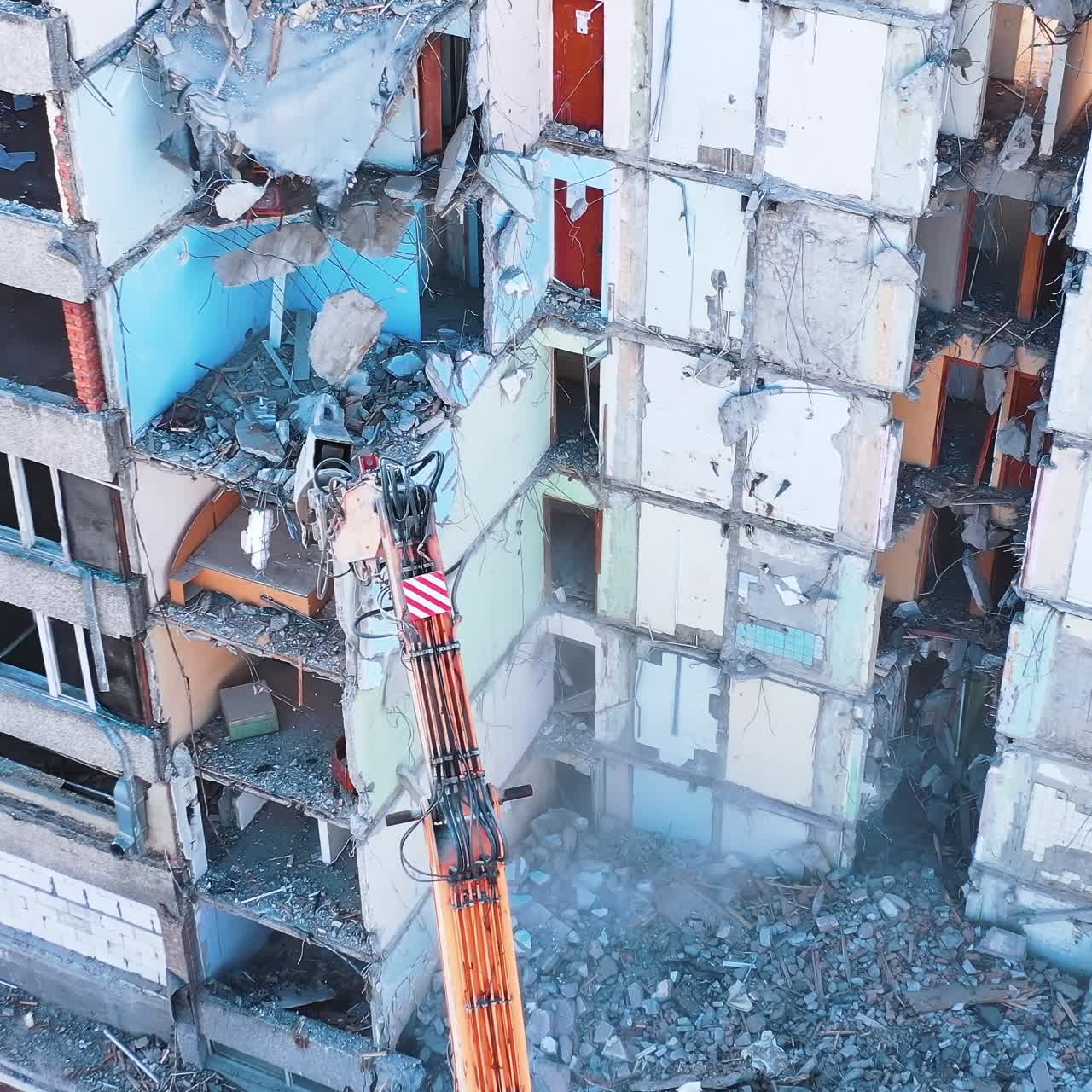 Demolishing machine breaks the walls and floors of the big ruined building. Aerial view of the deconstruction site