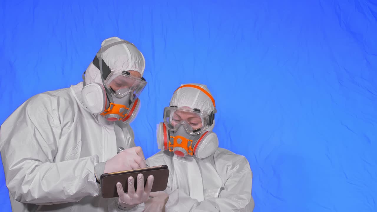 científico virólogo en respirador hace escribir en una tableta con lápiz. hombre y mujer con máscara médica protectora. clave de croma azul.
