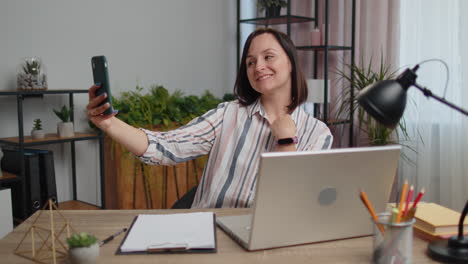 Young-woman-blogger-taking-selfie-portraits-on-smartphone-for-social-media-vlog-while-working-home