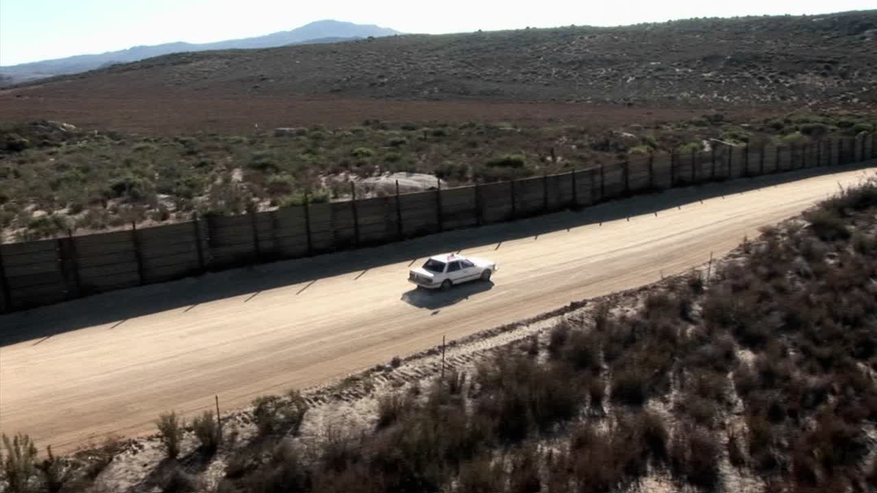 um carro dirige ao longo de uma estrada cercada por uma cerca alta