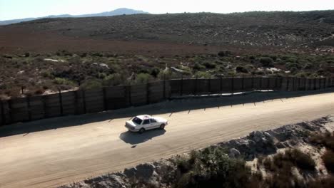 A-car-drives-along-a-road-bordered-by-a-high-fence