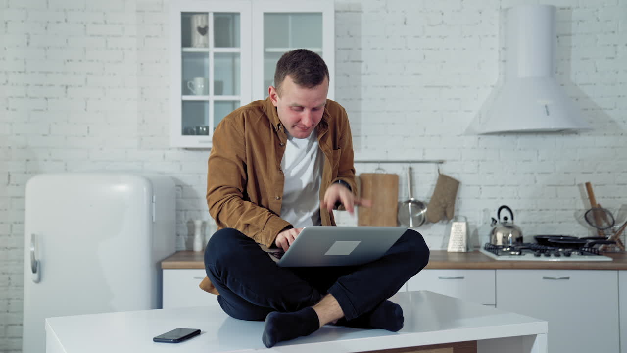 Young man pressing buttons on a laptop at home. Funny face of a businessman after working long hours on a computer. Tired mad man on the table at home with a laptop.