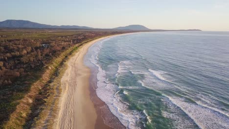 Vista-Aérea-De-Una-Playa-Aislada-En-Nueva-Gales-Del-Sur,-Australia,-Con-Olas-Largas-Y-Tranquilas-Rompiendo-La-Costa-Al-Atardecer