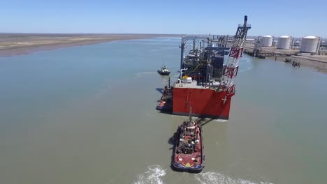 vista aérea del buque de carga que llega al puerto con la ayuda de remolcadores