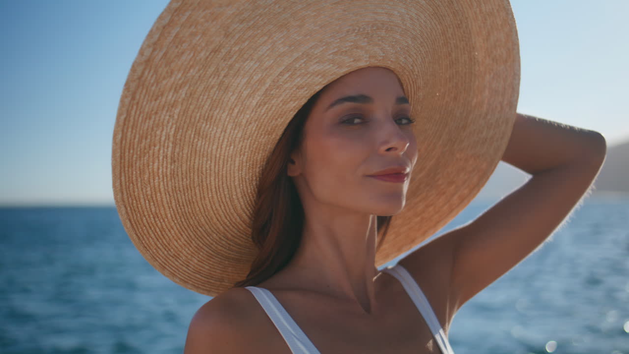 Turista sereno si gode la luce del sole sulla spiaggia con cappello di paglia in primo piano