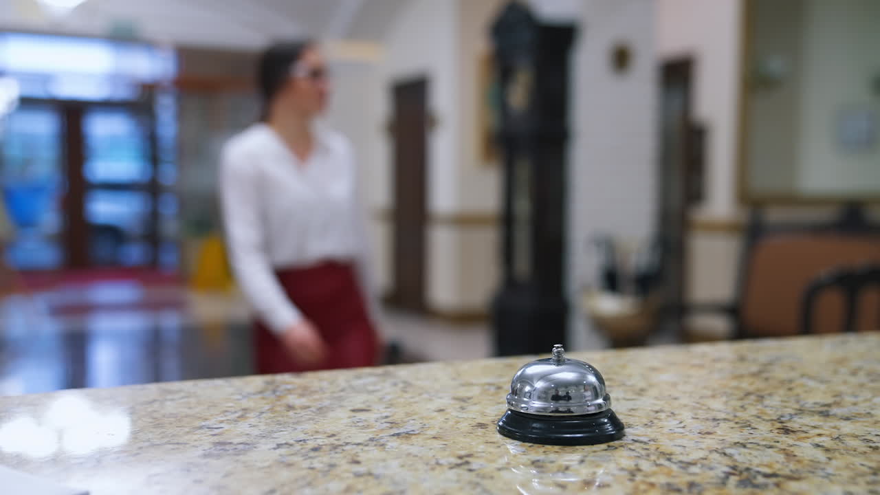Bell button in hotel. Blurred background of woman with suitcase pressing hotel bell on table. Female client coming to a receptionist desk in vestibule for check in or check out. Tourism and travelling.
