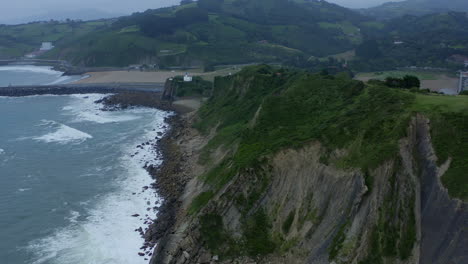 Die-Nach-Oben-Geneigte-Luftschwenkung-Zeigt-Grasbewachsene-Klippenränder-über-Dem-Strand-Von-Itzurun