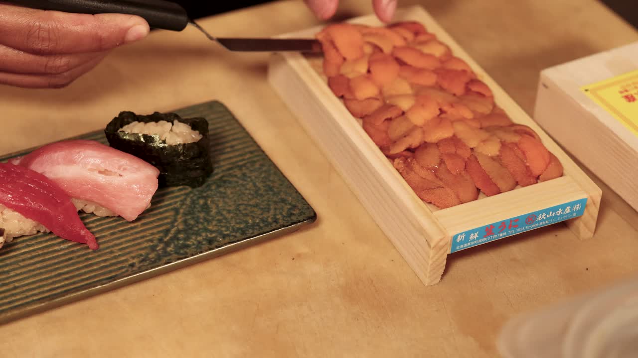 Primo piano di uno chef che sistema con cura dei ricci di mare freschi sul sushi, sotto la calda luce di un ristorante