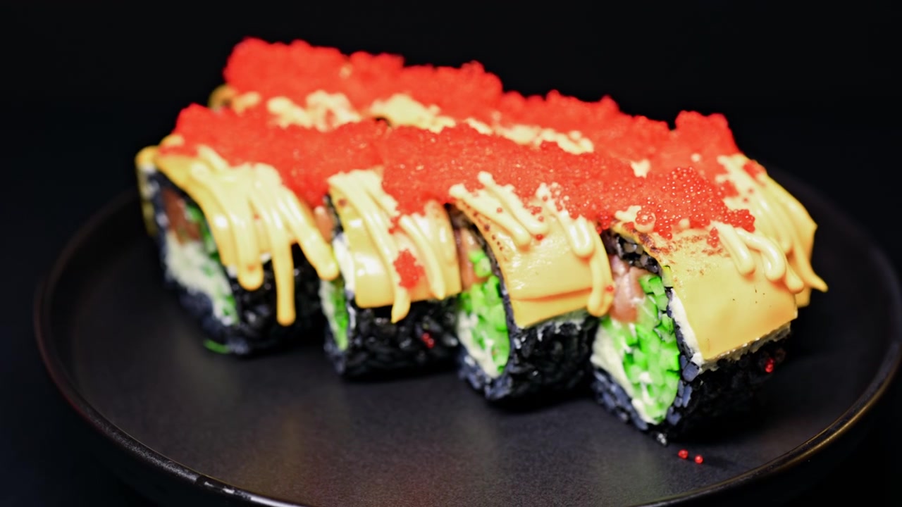 Sushi-Rollen mit schwarzem Reis, Fisch, Gemüse und Soße, ansprechend auf einem schwarzen Teller in einem Restaurantambiente arrangiert.