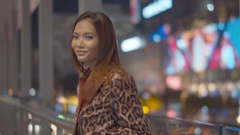 gorgeous asian woman smiles and flirts with the camera under the bright night lights of the city