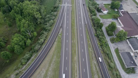 Toma-En-ángulo-Alto-Sobre-La-Autopista-Y-La-Intersección-De-Carreteras-Con-Edificios-En-Un-Lado-Y-Una-Exuberante-Vegetación-Verde-En-El-Otro-Lado-Durante-El-Día