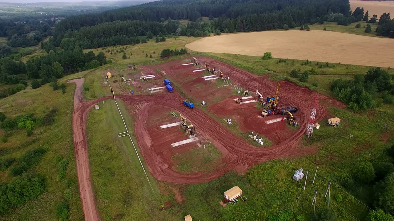 panorama aéreo de las bombas de petróleo en el clúster de campos petrolíferos. mañana de verano, las bombeas de petróleo de trabajo y la plataforma de perforación entre los campos y bosques.