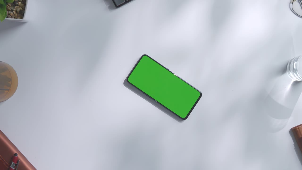 vista de arriba hacia abajo de una computadora portátil con pantalla verde simulada pantalla chromakey en un escritorio de oficina de madera al lado de la libreta con bolígrafos, gafas y un vaso de agua.