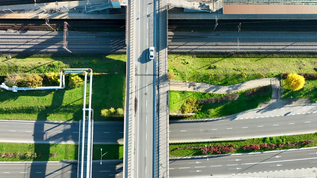 Aerial top view of cars driving on bridge above railway tracks and green city landscape