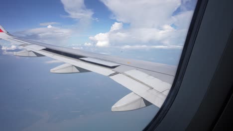 view from airplane window showing wing and clouds, with clear skies and earth far below