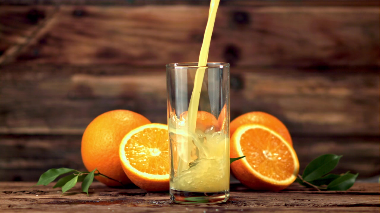 Fresh Orange Juice Poured into a Glass with Oranges on a Wooden Background