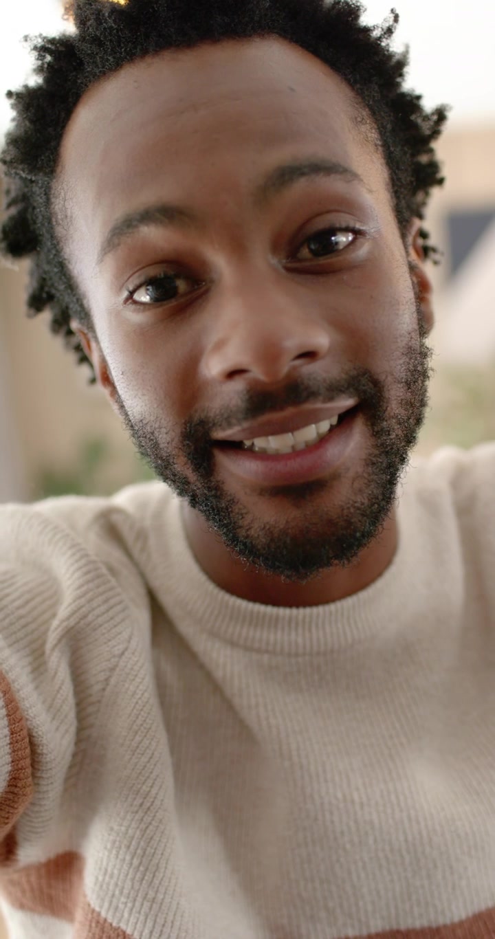 Vertical video: African American man filming message holding smartphone at home, smiling, gesturing