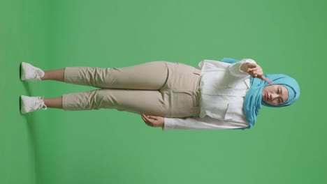 full body of asian muslim woman disapproving with no index finger sign while standing in the green screen background studio