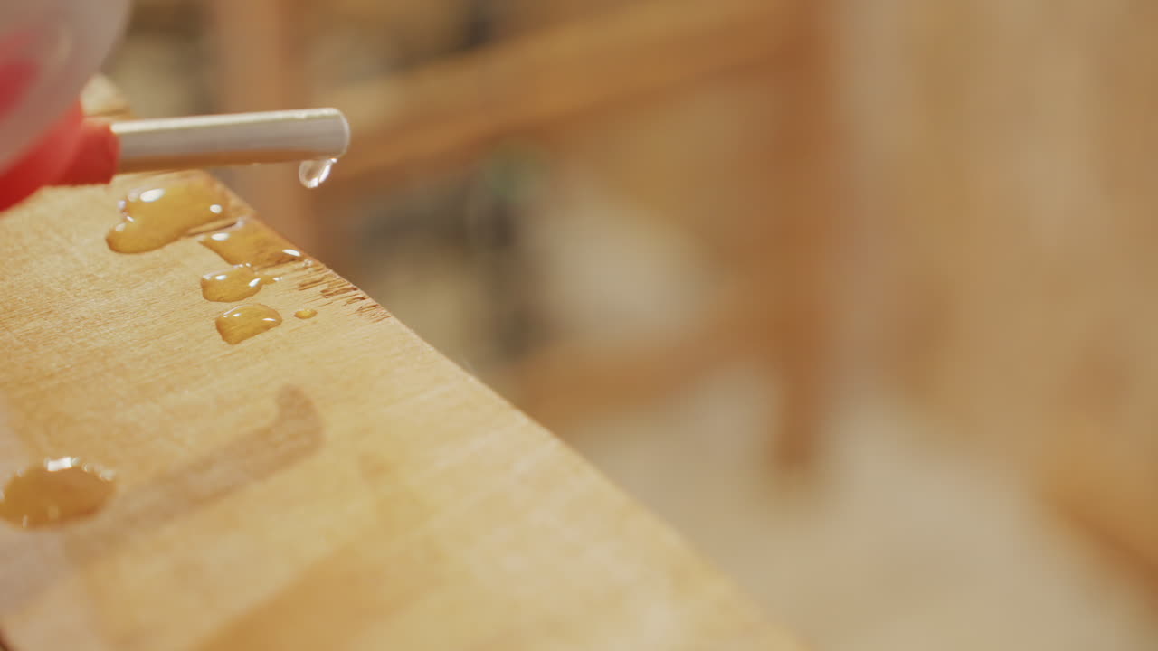 nozzle dripping liquid onto wood macro, golden droplets forming on weathered plank, shallow depth of field with soft bokeh, studio ambience, textured grain and glossy reflections, slow motion study