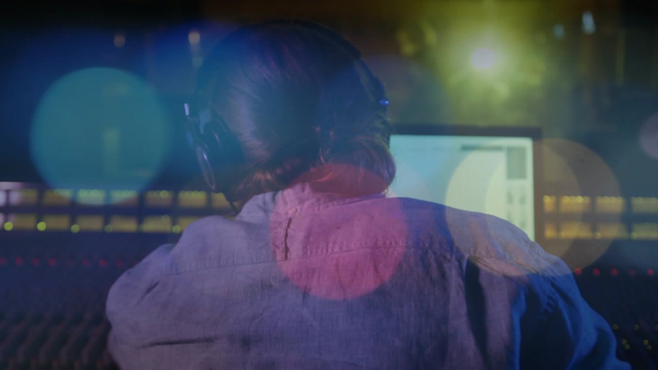 Music producer starting playback, tweaking faders while watching waveform, tuning mix amid bokeh