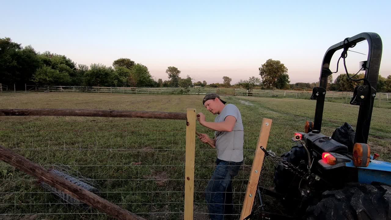 Man With A Hammer Securing A Nail, Repairing A Farm Fence In Flat Rock, Michigan, USA - Medium Shot