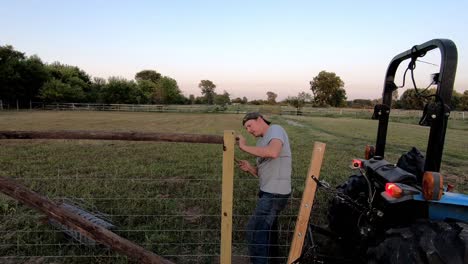 man with a hammer securing a nail, repairing a farm fence in flat rock, michigan, usa - medium shot