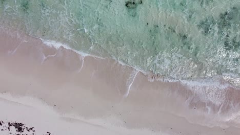 Aerial-view-looking-down-of-clear-sea-waves-crashing-onto-a-white-sand-beach-while-drone-moves-towards-the-sea-on-Cozumel-Island,-Mexico