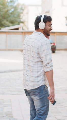happy man tourist in wireless headphones choosing listening disco music on smartphone on street