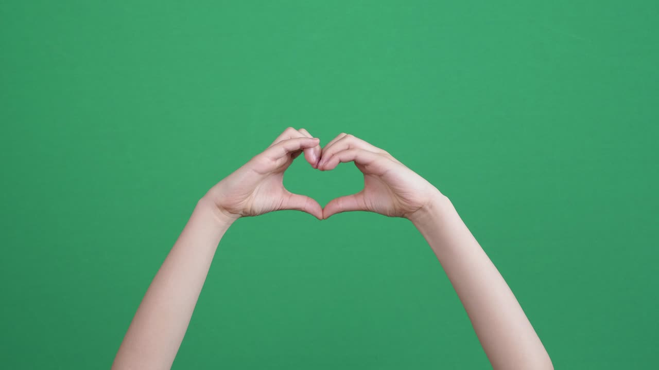 primer plano de las manos de los niños haciendo un gesto en forma de corazón en la pantalla verde con fondo de cromakey. la persona forma forma de corazón usando sus dedos