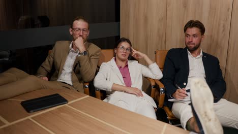 two guys in business suits and a girl in a white jacket and pink shirt are sitting at a table with their feet on the table. tired group of workers in a modern office